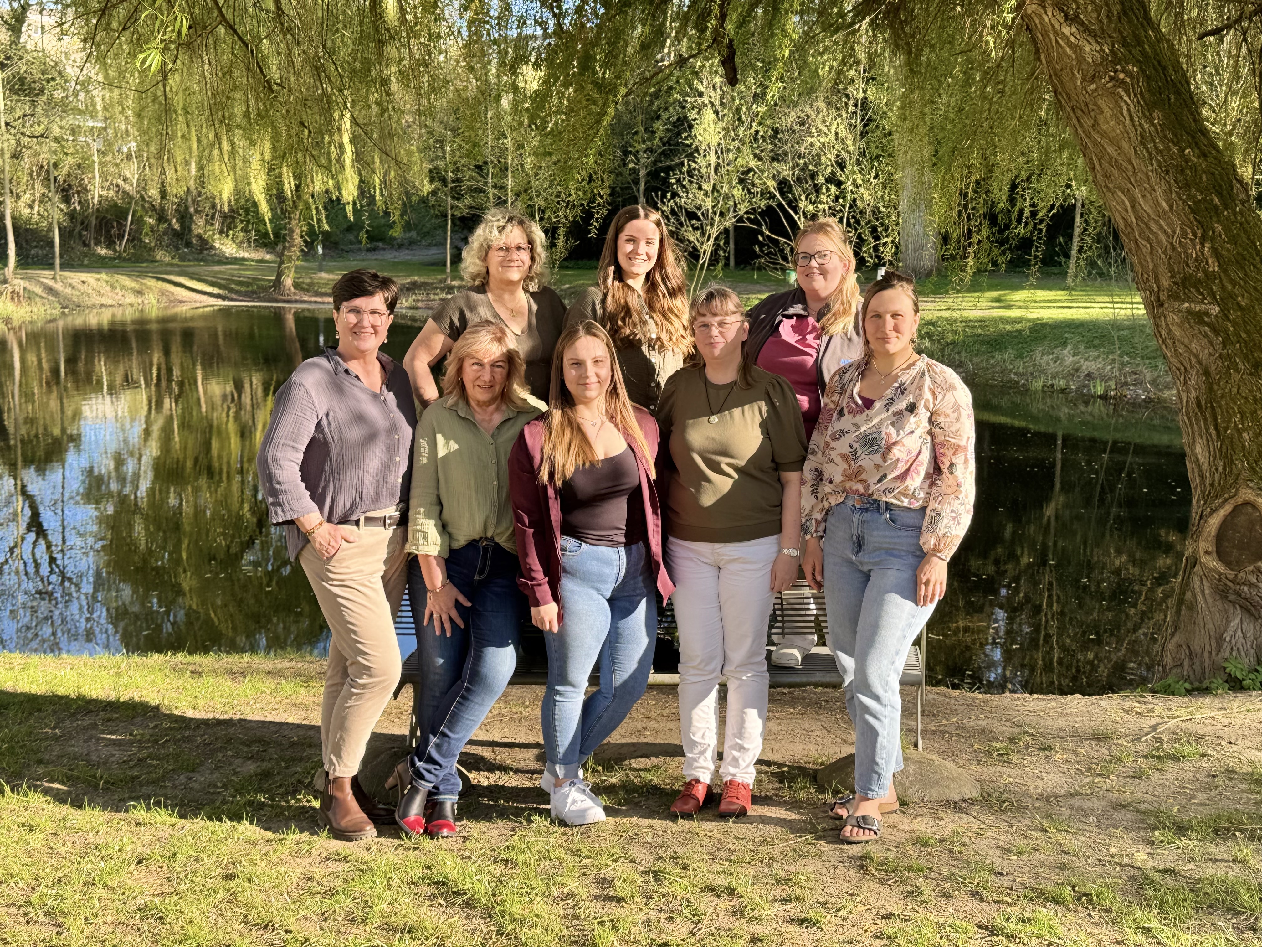Acht lächelnde Frauen in warmem Licht vor einem Teich