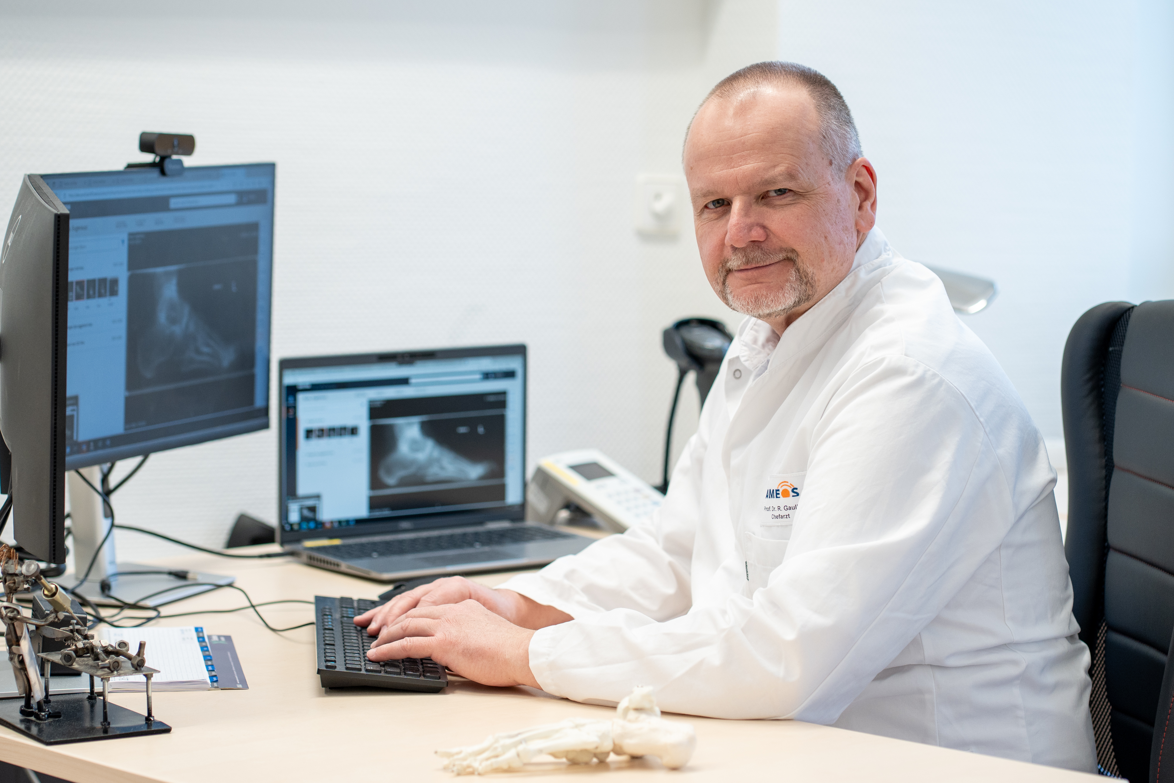 Professor Gaulke sitzt am Schreibtisch und schaut sich ein MRT-Bild von einem Fuß an.