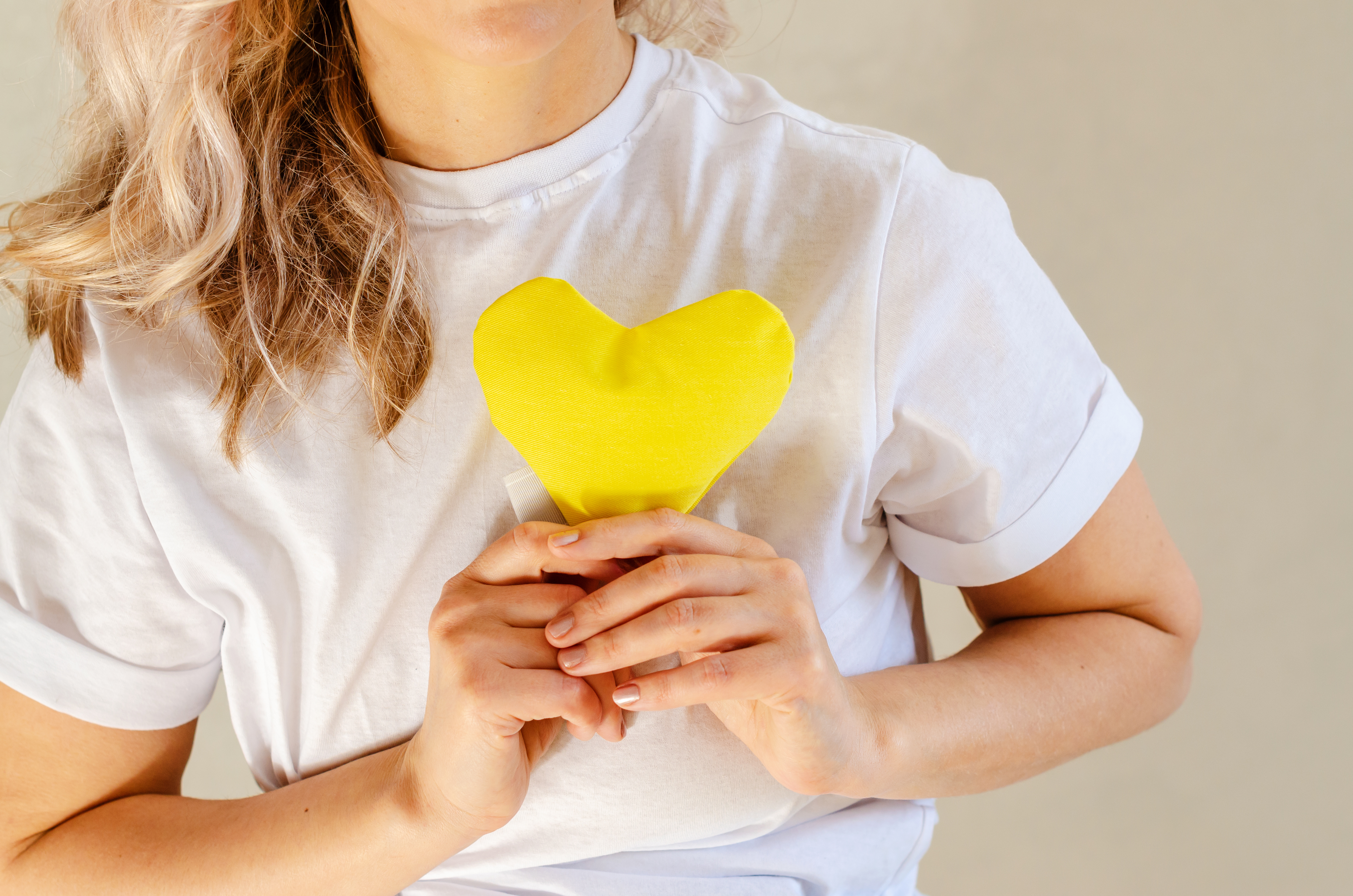Frau hält ein gelbes Herz vor ihre Brust.