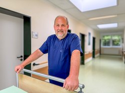Torsten Masella blickt fröhlich in die Kamera und schiebt ein Patientenbett.Middelburg (© AMEOS).