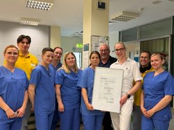 Pflegepersonal und ärztliches Personal auf der Regionalen Stroke Unit hält lächelnd ein Zertifikat in die Kamera.