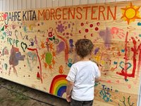 Kind vor bemaltem großem Schild aus Sperrholz. 