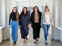 Vier Frauen laufen nebeneinander einen Flur entlang.